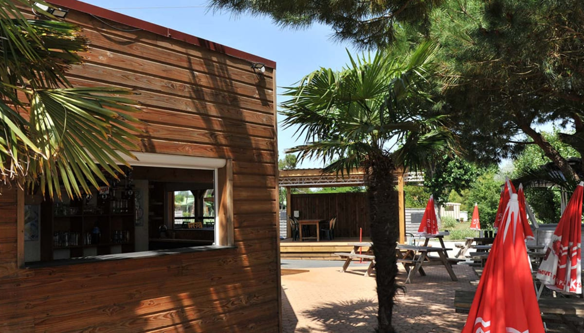 Bar en bois de la guinguette avec tables de pique-nique et palmiers, Camping Le Dauphin