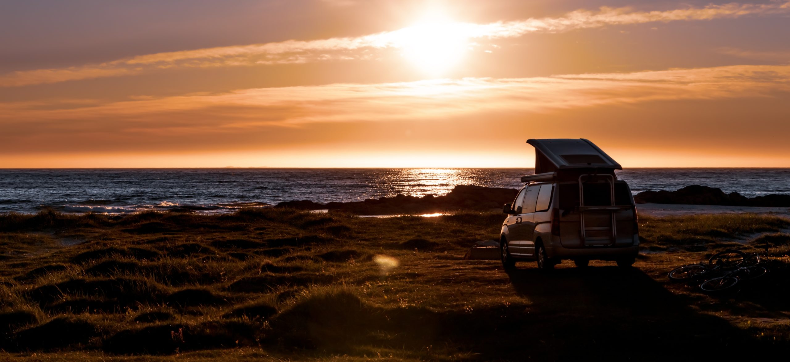 Van aménagé à toit relevable stationné face à la mer au coucher du soleil